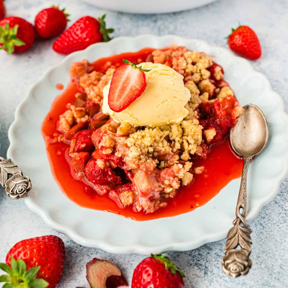 hellblauer Teller mit Erdbeer-Rhabarber-Crumble und Vanilleeis darauf